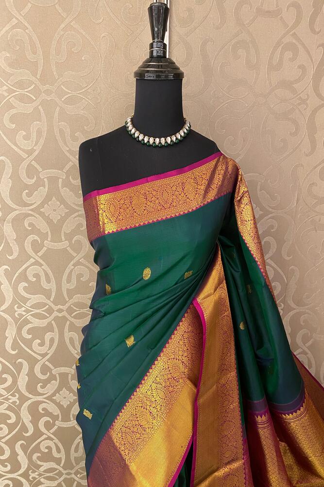 Bottle green pure Kanjeevaram silk saree with traditional motifs and an unstiched blouse, displayed on a hanger.