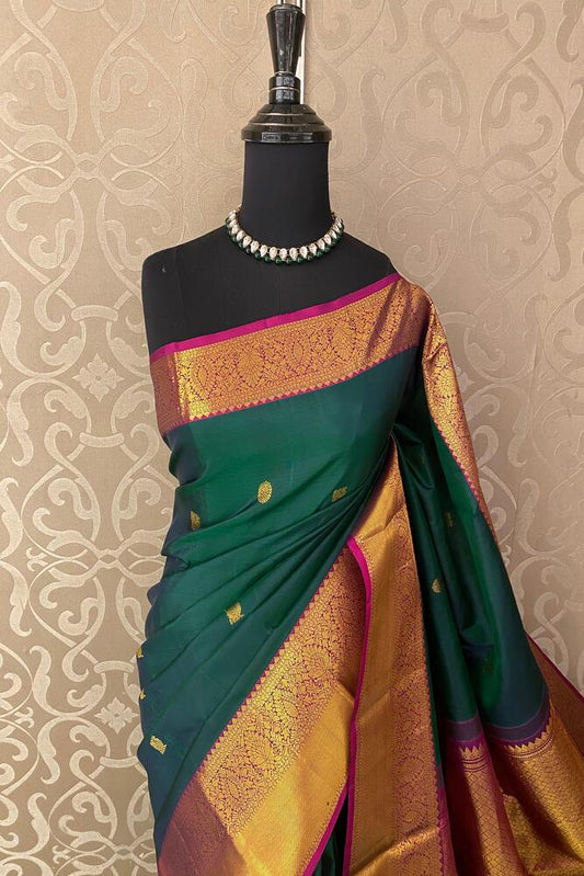 Bottle green pure Kanjeevaram silk saree with traditional motifs and an unstiched blouse, displayed on a hanger.